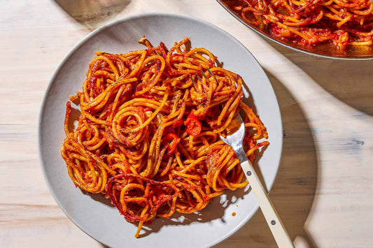 An overhead photo of a plate of spaghetti in a red sauce and topped with seasonings.