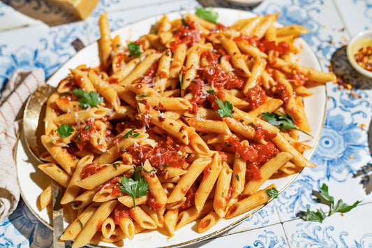 A serving dish topped with penne pasta, crushed tomatoes, and topped with fresh herbs.