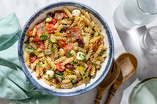 An overhead photo of a large serving bowl filled with pasta salad and topped with fresh herbs.