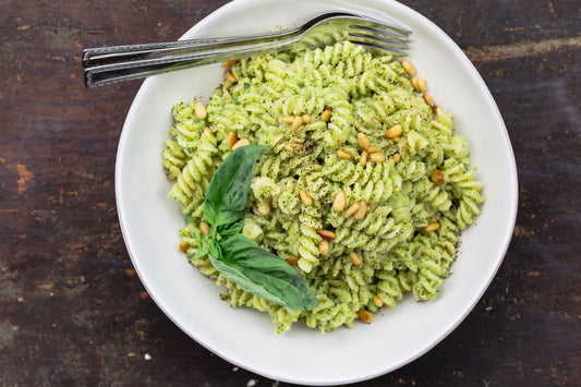 An overhead photo of a bowl of fusilli pasta topped with fresh basil and a fork inside the bowl.