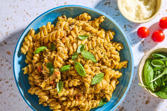 An overhead photo of a bowl of fusilli in an almond pesto sauce and topped with fresh herbs.
