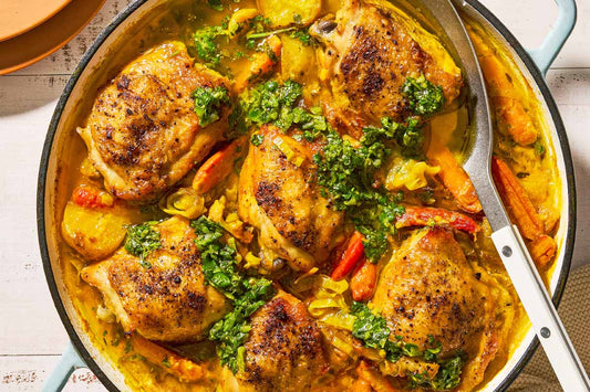 An overhead photo of a dutch oven with 6 chicken thighs mixed with vegetables in a creamy sauce.