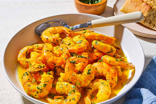 A bowl of poached shrimp topped with fresh herbs and a serving spoon.