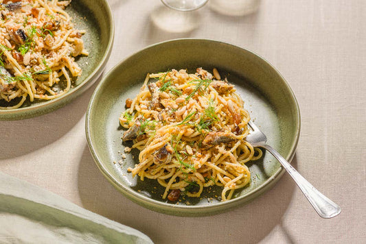 A plate of spaghetti topped with sardines and fresh herbs with a fork on the side.