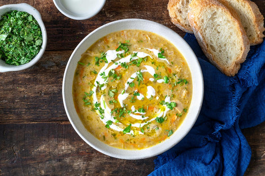 An overhead photo of a bowl of soup topped with fresh herbs aside sliced bread and a bowl of fresh herbs.