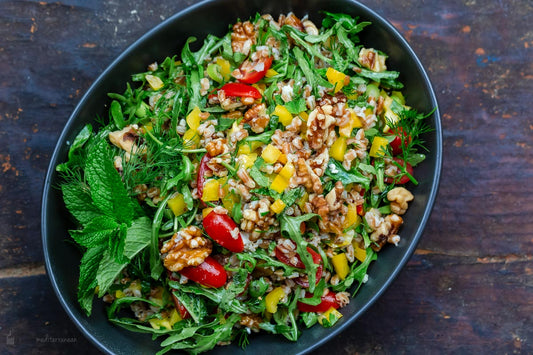 An overhead photo of a serving dish topped with farro salad with arugula, feta, and walnuts.