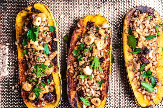 An overhead photo of three halves of delicata squash stuffed with farro and topped with fresh herbs.