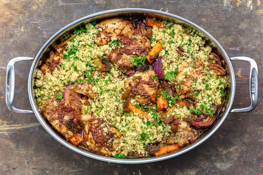 An overhead photo of a large baking dish filled with couscous, chicken, vegetables, and fresh herbs.