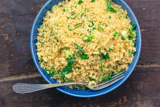 An overhead photo of a bowl filled with cooked couscous and topped with fresh herbs with a fork.