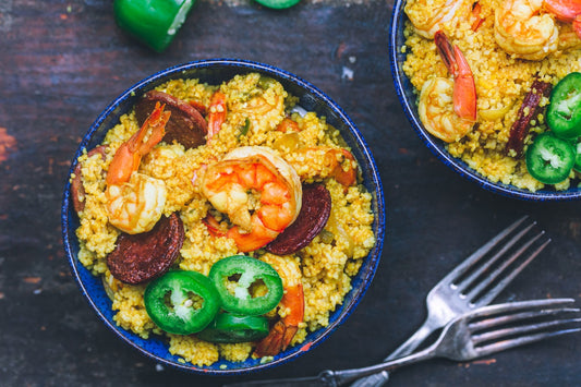 An overhead photo of two bowls filled with couscous, shrimp, and chorizo topped with sliced jalapenos.