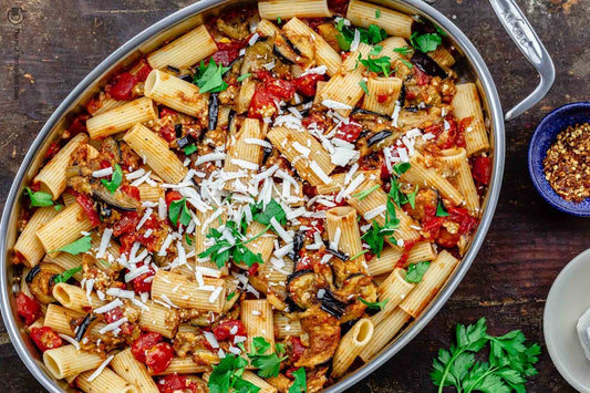 An overhead photo of a baking dish filled with rigatoni pasta topped with fresh herbs and parmesan cheese.