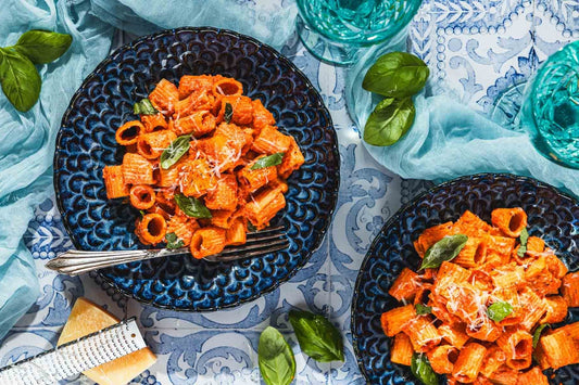 An overhead photo of two bowls filled red with rigatoni pasta in a roasted red pepper sauce.