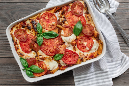 An overhead photo of a baking dish filled with baked rigatoni and topped with melted mozzarella and fresh basil.