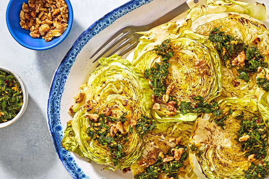 An overhead photo of a plate topped with cabbage steaks and topped with chopped walnuts and chermoula sauce.