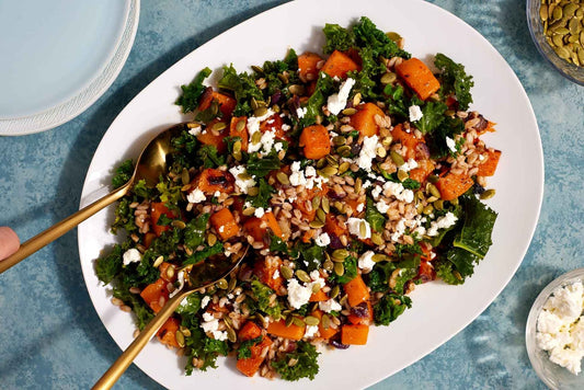 Butternut squash salad on a serving platter with gold serving utensils.