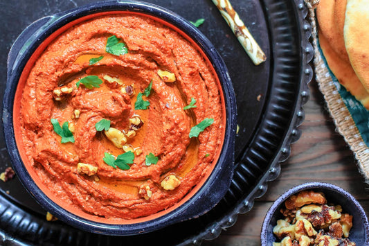 An overhead photo of a bowl of roasted red pepper dip and topped with fresh herbs and chopped nuts.