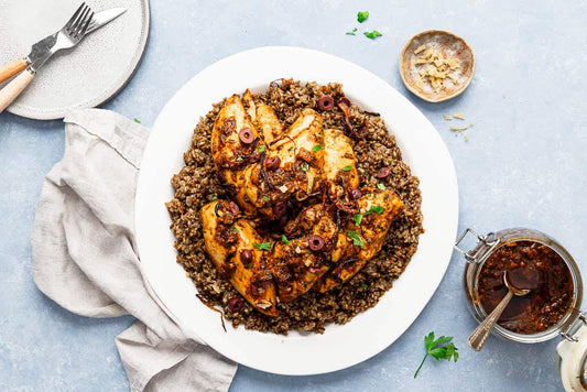 An overhead photo of a large white dish topped with freekeh grains, chicken breasts, and fresh garnishes.