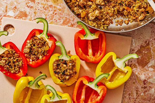 A cutting board topped with halved yellow and red peppers stuffed with a grain filling.