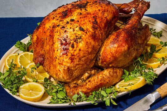 A large serving dish topped with a roasted Thanksgiving turkey and garnished with greens and lemon slices.