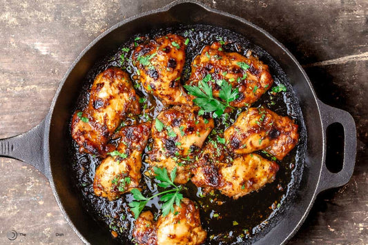 An overhead photo of a cast iron skillet filled with chicken thighs in a balsamic sauce and topped with fresh herbs.
