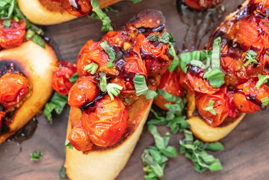 A close up of 3 pieces of bruschetta topped with tomatoes, balsamic vinegar, and fresh herbs.