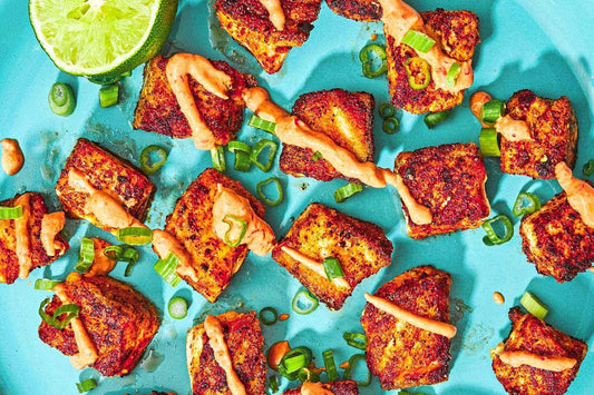 A blue plate topped with crispy salmon cubes and garnished with fresh herbs and an orange sauce with a half of a lime off to the side.