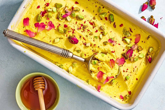 An overhead photo of a baking dish filled with yellow ice cream and toppings with a bowl of honey off to the side.