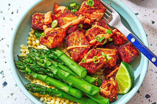 A blue plate topped with crispy salmon cubes and garnished with fresh herbs and an orange sauce with a half of a lime off to the side.