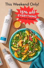 A promotional flat-lay featuring several white bottles of The Mediterranean Dish olive oil arranged around a turquoise plate of fresh salad with peach slices, crumbled cheese, and an orange fork. Large text at the top reads 'This Weekend Only! 15% off EVERYTHING No Code Needed'.