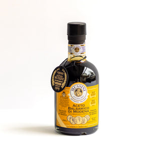A bottle of Mussini Aceto Balsamico di Modena (Molden Balsamic Vinegar) with a black cap, dark liquid inside, and a bright yellow label featuring gold details and a black circular authenticity seal.