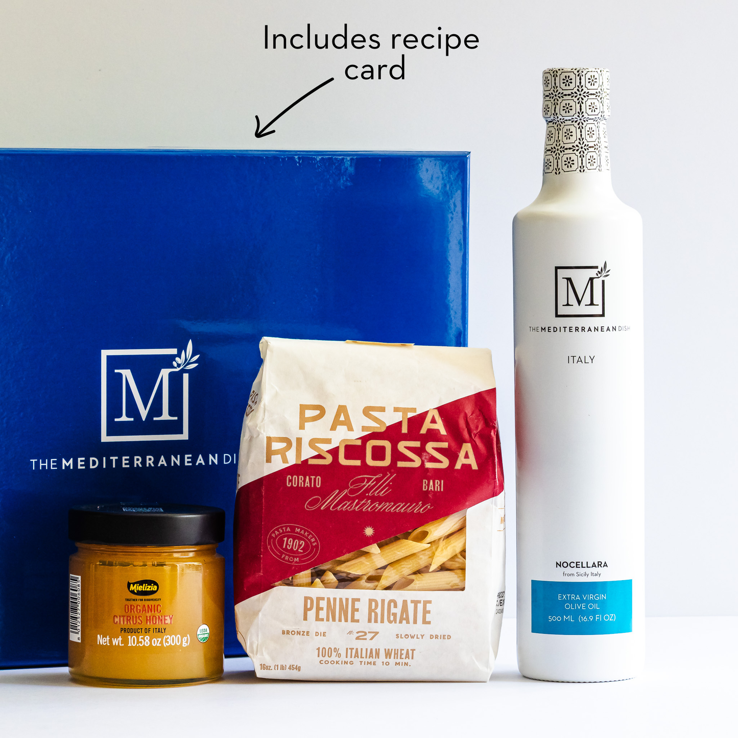 Assorted food products including pasta, olive oil, and a jar with a recipe card on a white background.