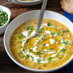 Two bowls of soup with a spoon, garnished with cream and herbs, on a wooden surface.