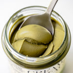 Jar of green pistachio cream with a spoon inside on a white background