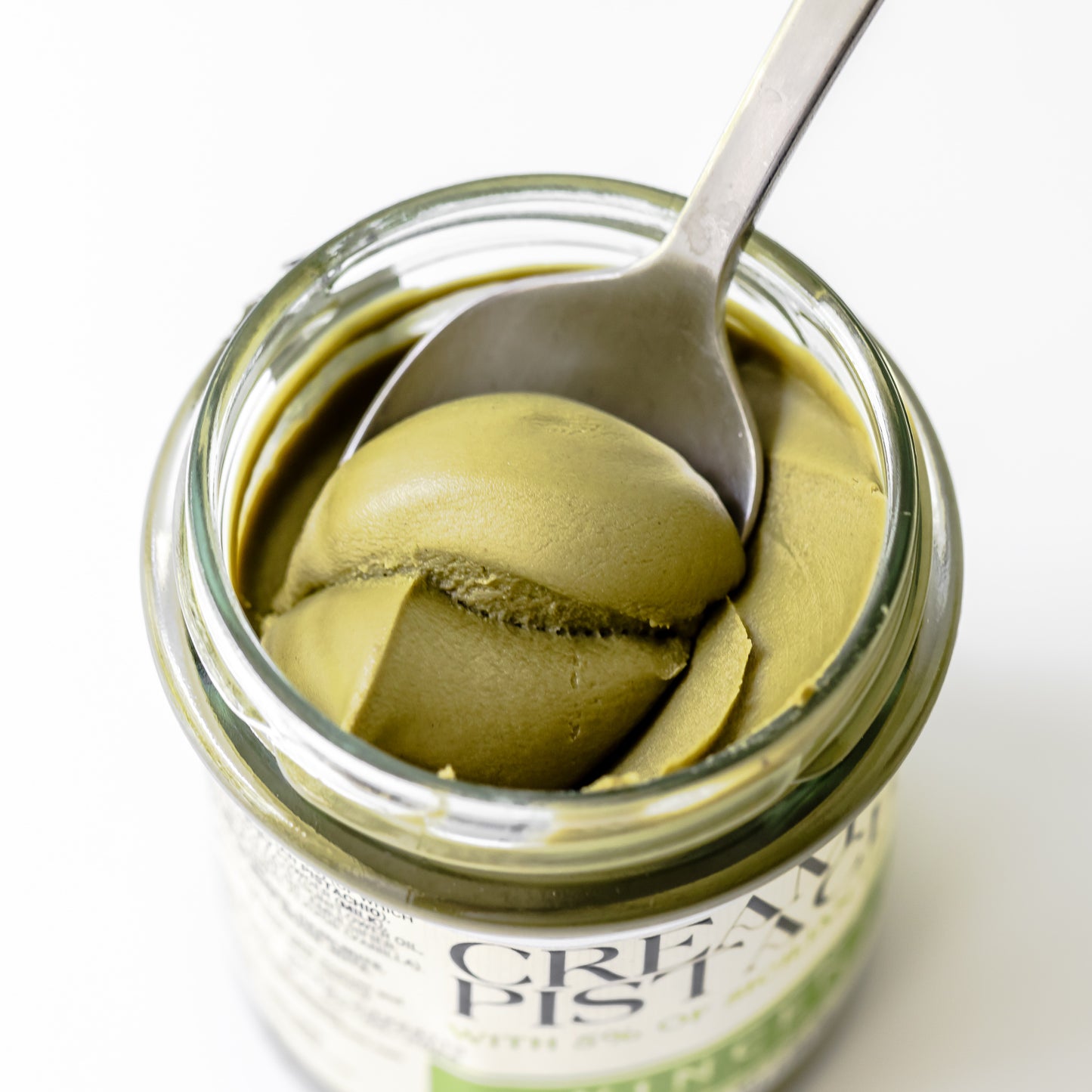 Jar of green pistachio cream with a spoon inside, on a white background