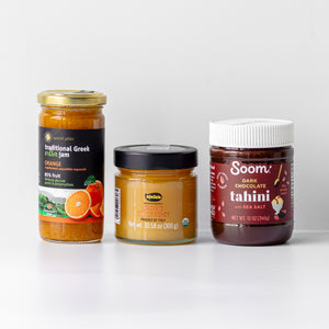 A bundle including three jars of orange jam, honey, dark chocolate tahini, set against a clean white background.