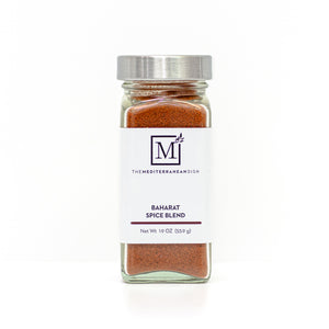 A glass spice jar filled with baharat, featuring a white label with the brand logo 'The Mediterranean Dish' and a silver metal lid, set against a clean white background.