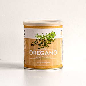A canister of Greek Oregano dried & crushed spice blend on a clean white background. The label features a kraft paper texture with a green oregano herb illustration and white text.