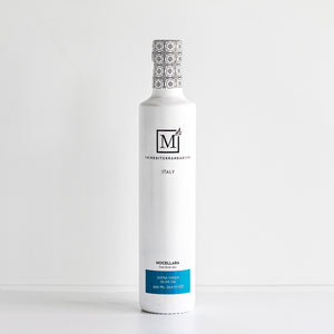 A white glass bottle of Nocellara extra virgin olive oil by The Mediterranean Dish featuring a black and white patterned cap and a blue label at the bottom, set against a clean white background.
