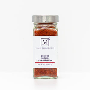 A glass spice jar filled with smoked paprika, featuring a white label with the brand logo 'The Mediterranean Dish' and a silver metal lid, set against a clean white background.