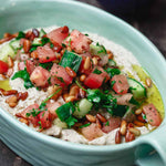 Baba ganoush in dish, topped with tomatoes, cucumbers, parsley and pine nuts.