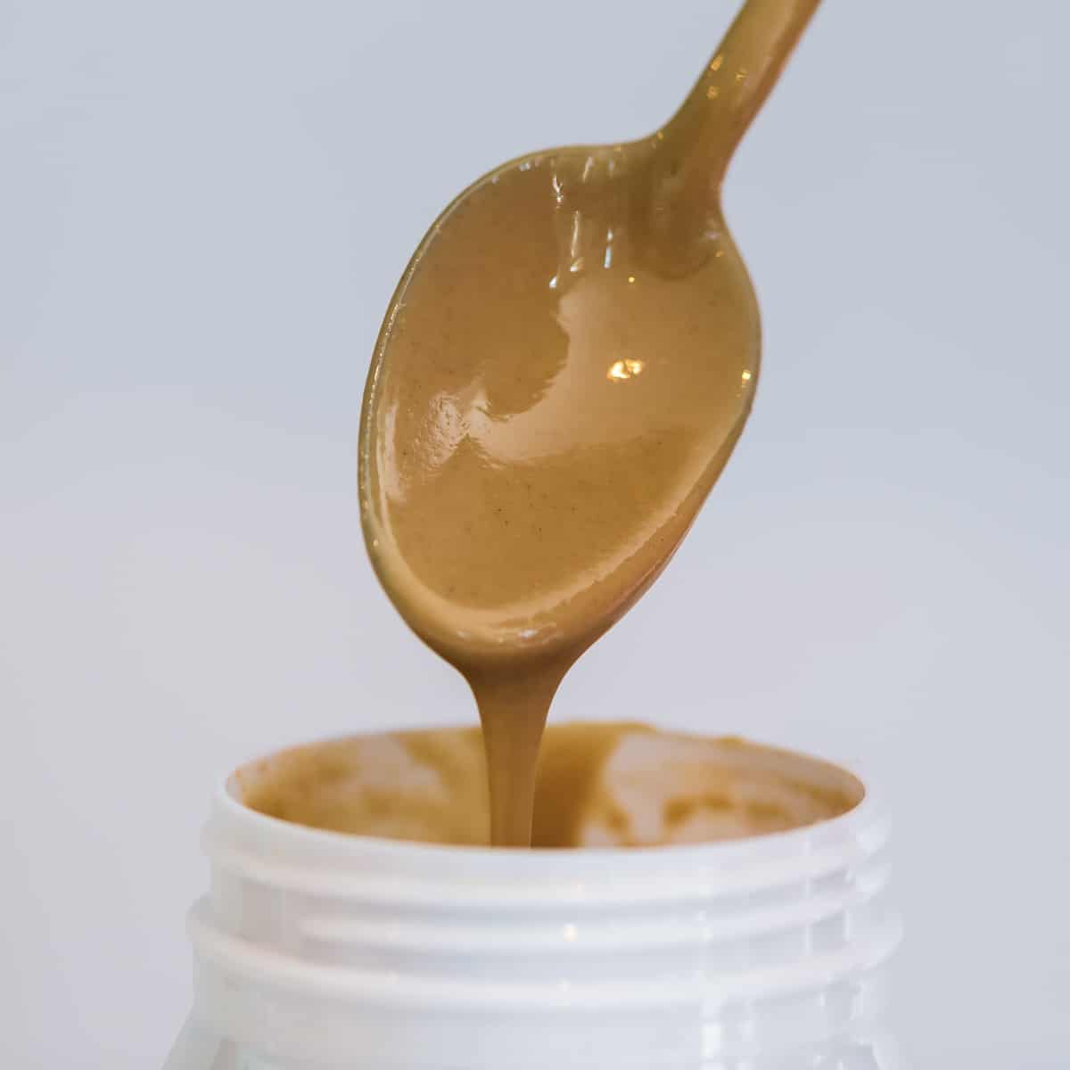 Spoon with tahini pouring into jar